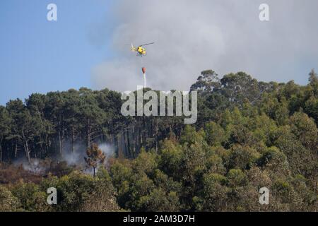 La lutte contre l'hélicoptère pompiers jaune feu de forêt en Côte d'Astoria, Espagne Banque D'Images