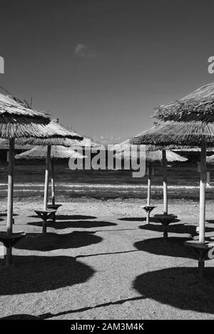 Parasols en rangées jetant des ombres sur le sable sur une plage vide en hiver, situé à Kavouri, Athènes. Banque D'Images