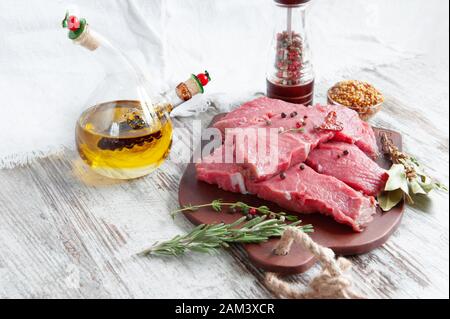 Des portions de viande préparées pour la marination se trouvent sur un tableau d'argile avec des épices, de l'huile d'olive et des herbes aromatiques. Gros plan. Banque D'Images