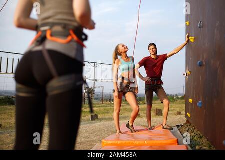 Instructeur homme guide une femme blanche assez mince sur le mur d'entraînement de l'escalade à l'extérieur. Style de vie sain et concept de loisirs. Banque D'Images