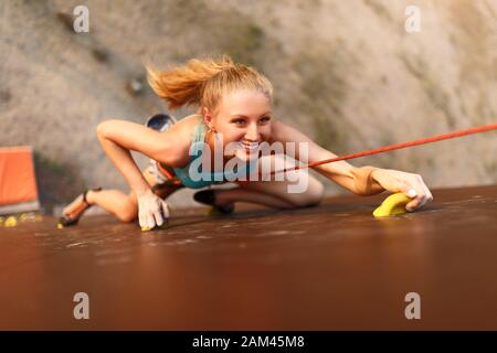 Concept de réussite forte pour les femmes et les entreprises. Jeune femme blanche et jolie pratiquant l'escalade sur mur de roche artificiel à l'extérieur. Blonde sportive et mince Banque D'Images