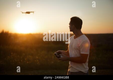 Silhouette d'un homme pilotant drone dans l'air avec une télécommande dans ses mains au coucher du soleil. Pilote prend des photos aériennes et des vidéos avec quadricopter Banque D'Images