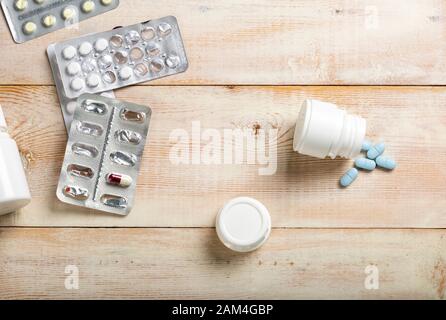 Pilules bleues déversées à partir d'une bouteille en plastique blanc. Différentes boîtes et flacons de médicaments en arrière-plan. Banque D'Images