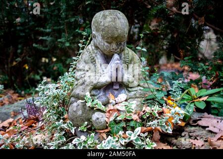 Statue en pierre d'un Bouddha légèrement pleurant assis sur un grave sourarrondi par les plantes Banque D'Images