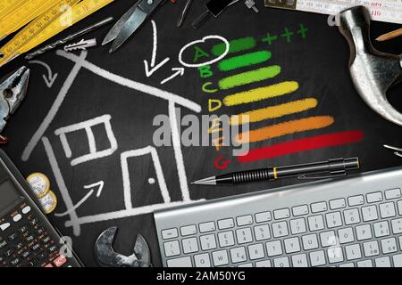 Rendement Énergétique De La Maison. Tableau noir avec dessin de craie, outils de travail, calculatrice et clavier d'ordinateur. Projet de maison écologique Banque D'Images