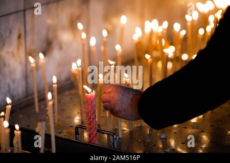 Détails avec les mains d'une vieille femme illuminant une bougie à l'intérieur d'une église orthodoxe chrétienne en Roumanie. Banque D'Images