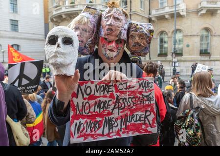 Londres, Royaume-Uni. 11 janvier 2020. Un manifestant à Portland place, Londres, tient un masque de crâne et une pancarte peinte à la main indiquant « PLUS DE GUERRES PÉTROLIÈRES, PLUS D’ASSASSINATS, PLUS DE MEURTRE de MPS ». La coiffe présente des visages imprimés avec de la peinture rouge ressemblant au sang, symbolisant l'opposition à la guerre, la violence politique et la complicité du gouvernement. La manifestation fait référence à l'assassinat du général iranien Qassem Soleimani et appelle à la paix et à la responsabilisation. Les manifestants défilent de la BBC à Trafalgar Square après le meurtre de Soleimani, appelant à la paix et à la non-guerre avec l'Iran. Penelope Barritt/Alamy Live News Banque D'Images