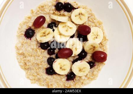 Petit-déjeuner à l'avoine avec de la banane, les bleuets et les raisins rouges, isolé sur fond blanc et photographié à partir de juste au-dessus. Banque D'Images