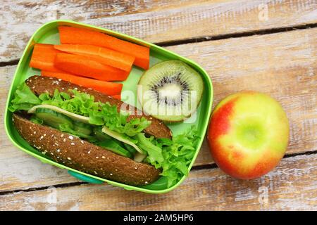 Boîte à déjeuner saine contenant un rouleau de fromage de seigle, des bâtonnets croquants de carottes, des fruits kiwi et de la pomme Banque D'Images