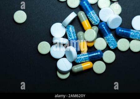 Tas de pilules colorées, médecine pharmaceutique comprimés et gélules sur fond noir. La prescription d'un traitement de soins de santé médicaments con Banque D'Images