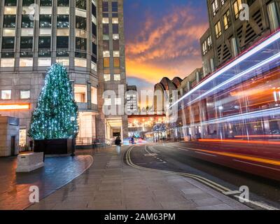 Bus rouge traditionnel en mouvement sur la route près de la place de Canary Wharf, décorée avec des arbres en vacances d'hiver de Noël au Royaume-Uni Banque D'Images