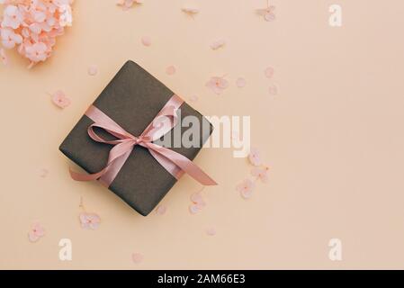 Boîte cadeau enveloppée dans du papier d'artisanat avec ruban rose sur fond orange pâle avec des fleurs d'hydracea. Banque D'Images
