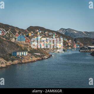 Des maisons colorées parsement les collines de la ville de pêcheurs de Kangaamiut, à l'ouest du Groenland. Icebergs du glacier de Kangia au Groenland nageant avec le ciel bleu Banque D'Images