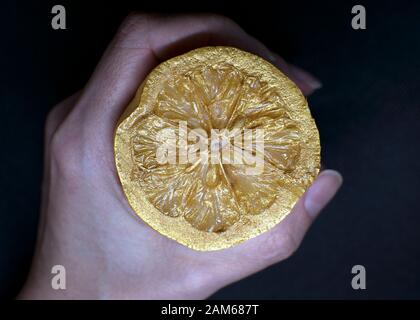 peint à la main avec de la peinture dorée, couper le citron. Citron jaune en main sur un fond sombre. Banque D'Images