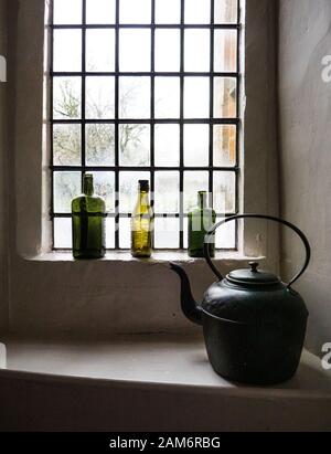 Bouteilles de gin vides colorées et une bouilloire à l'ancienne sur un rebord de fenêtre dans une ancienne auberge anglaise de coaching dans Les Cotswolds. Banque D'Images