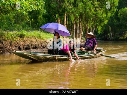 Les touristes asiatiques dans la sampan rongé par la femme locale portant l'aviron conique de chapeau avec les pieds, Tam Coc, Ninh Binh, Vietnam, Asie Banque D'Images