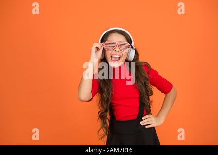 Piste froide. Fille avec lunettes arrière-plan orange. Événement et divertissement. Fille de fête. Accessoire de fête. Amuse-toi bien. Liste de lecture pour la fête. Concept de musique. Enfant porter des lunettes. Magasin de mode de lunettes. Banque D'Images