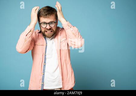 Homme barbu en furieux. Il gronte les dents, a levé les mains à la tête et regarde avec haine à la caméra. Espace de copie. Banque D'Images