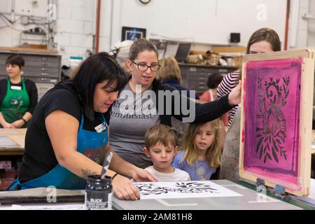 Artiste Bretagne Houk (gauche) guides membres de la famille à Burgess imprime à la Pratt Fine Arts Center le Samedi, Janvier 11, 2020. Mené par l'artiste Claire Jauregui pour la quatrième année consécutive, les membres du public ont été invités à contribuer à l'écran imprimer des affiches d'artistes locaux à l'appui de l'Womxn à venir Mars sur Seattle. Écran De soie dessins ont été fournies par les artistes Eileen Jimenez, Lynda Sherman et Leigh Riibe. Le rallye et mars, organisée par Womxn Seattle marche en avant, aura lieu le 18 janvier 2020. Banque D'Images