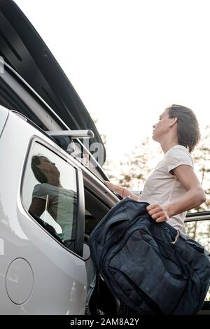 Une femme ciblée met les choses dans la galerie de toit d'une voiture ou dans une boîte de chargement. Préparation pour des vacances. Banque D'Images