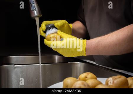 Laver et rincer les pommes de terre en préparation à la cuisson. Modèle avec gants en caoutchouc jaune jetables. Banque D'Images