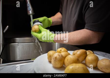 Laver et rincer les pommes de terre en préparation à la cuisson. Modèle avec gants en caoutchouc vert jetables. Banque D'Images