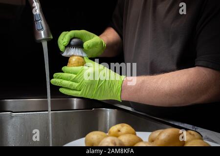 Gros plan sur le lavage et le rinçage des pommes de terre en préparation à la cuisson. Modèle avec gants en caoutchouc vert jetables. Banque D'Images