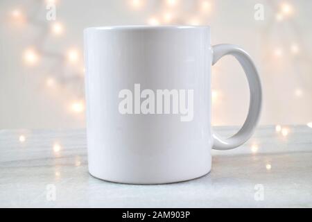 Une tasse à café de 11 oz repose délicieusement sur un fond de marbre avec des lumières de Noël blanches illuminant à l'arrière-plan. Ajoutez votre propre motif au mug. Banque D'Images