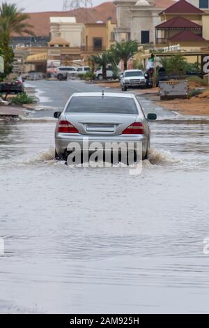 Voiture argent en traversant les eaux d'inondation dans la rue, ce qui fait de grandes éclaboussures d'eau dans un quartier résidentiel. Concept météo. (Portrait) Banque D'Images