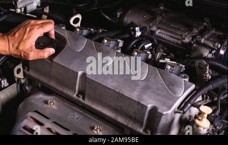 Main de technicien mécanicien auto entretien moteur et ouvrir le couvercle d'huile moteur sur la voiture dans le garage Banque D'Images