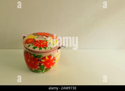 Gros pot en acier vintage avec motif fleuri dynamique sur une table blanche et un fond de mur de ciment. Apportez votre propre contenant, pas de conce en plastique à usage unique Banque D'Images