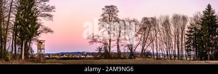 Panorama paysage avec tour de chasse après le coucher du soleil dans le paysage rural contre le ciel rose. Stand Deer près de Zettling Graz en Autriche. Banque D'Images