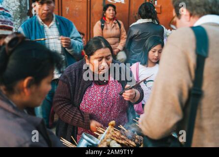 Urubamba, Région De Cuzco, Pérou - 29 Juillet 2010: Femme Au Barbecue Anticucho Skewers Streetfood Sur Une Rue De Marché Occupée À Urubamba. Banque D'Images