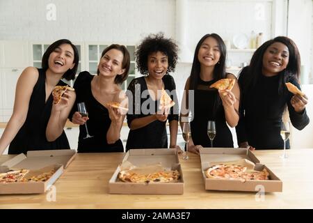 Des filles souriantes et diverses mangent de la pizza pour fêter la fête des jeunes filles à la maison Banque D'Images