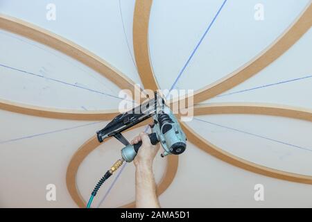 Installation de moulures décoratives sur le charpentier de plafond à l'aide d'un fragment de moulage de pistolet à ongles Banque D'Images