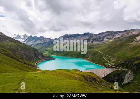 Vue sur le réservoir Lac de Moiry et le barrage en béton entouré de pâturages verts de montagne dans les Alpes de Pennine le jour nuageux de l'été. Sombre Banque D'Images