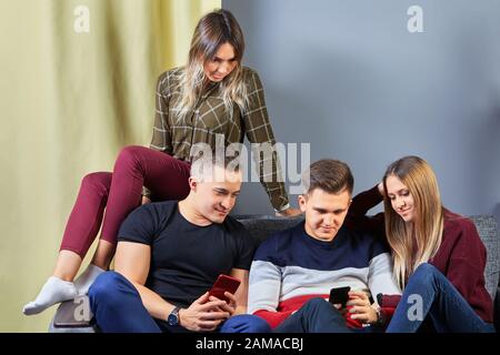 Fête d'étudiant dans le dortoir d'université. Jeunes hommes et femmes à une date romantique double regarder les écrans des téléphones mobiles. Des amis se sont réunis dans l'appartement A Banque D'Images