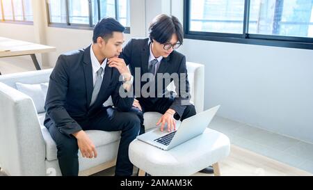 Un groupe de 2 hommes d'affaires travaillent sérieusement avec des ordinateurs au bureau. Banque D'Images