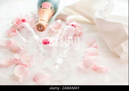 Verres à champagne en cristal de mariage sur une serviette en satin avec une bouteille de champagne et des pétales de rose Banque D'Images