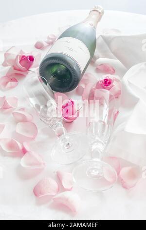 Verres à champagne en cristal de mariage sur une serviette en satin avec une bouteille de champagne et des pétales de rose Banque D'Images