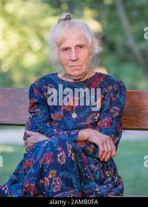 Élégamment vêtue, une vieille femme est assise sur un benchis parc assis sur un banc de parc. La Pologne. Banque D'Images