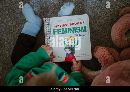 Jeune enfant lisant « Mon premier livre du féminisme (pour les garçons) par Julie Merberg Banque D'Images