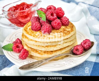 Une pile de crêpes décorées de framboises mûres et de sauceboat avec de la confiture en arrière-plan Banque D'Images