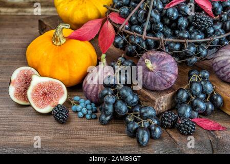 Raisins noirs dans un panier et figues mûres, framboises rouges, citrouille orange et mûres avec feuilles d'automne sur fond de bois Banque D'Images