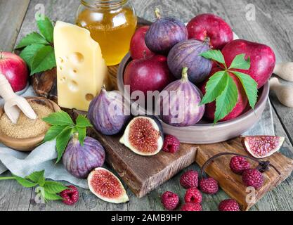 Les figues mûres, la framboise rouge et les pommes, le sucre de canne, le miel et un fromage sur l'ancien plateau de coupe ainsi que les feuilles vertes se trouvent sur l'ancienne table en bois Banque D'Images