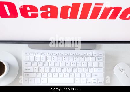 Texte affiché sur le moniteur, Date limite. Un bureau avec un clavier d'ordinateur et une tasse de café. Concept d'entreprise, vue de dessus Banque D'Images