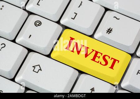 Un clavier avec Invest écrit en lettres rouges sur une touche d'entrée jaune. Concept d'investissement. Angleterre, Royaume-Uni, Grande-Bretagne Banque D'Images