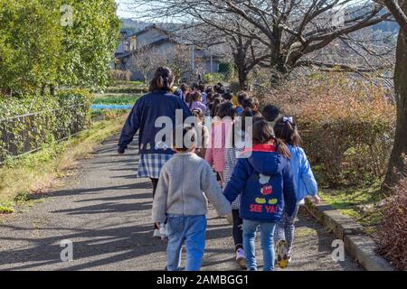 Les écoliers japonais en vêtements colorés marchent avec leur professeur dans la rue en hiver, Kanazawa, préfecture d'Ishikawa, Japon occidental. Banque D'Images