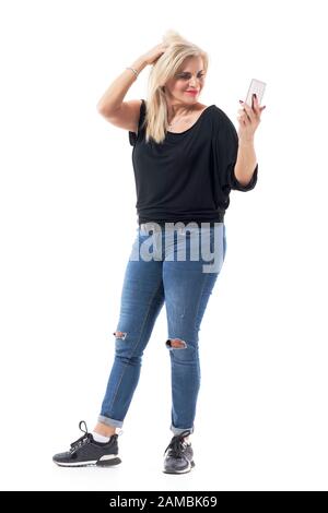 Une femme moderne blonde moderne et amusante d'âge moyen prenant des photos selfie avec smartphone. Longueur totale du corps isolée sur fond blanc. Banque D'Images