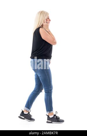 Une femme d'âge moyen qui s'inquiétait sérieusement de parler au téléphone en marchant et en regardant vers le bas. Vue latérale. Longueur totale du corps isolée sur fond blanc. Banque D'Images